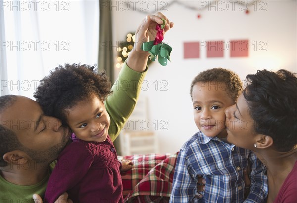 Black father holding mistletoe over daughter's head