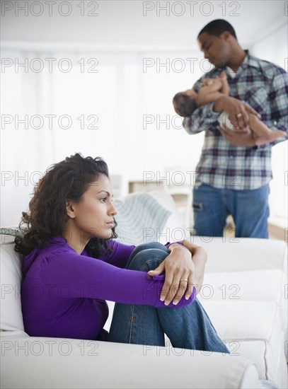 Sad mother with father holding baby in background