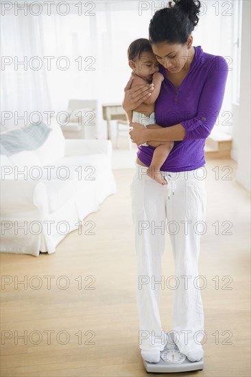 Mother holding baby and weighing herself