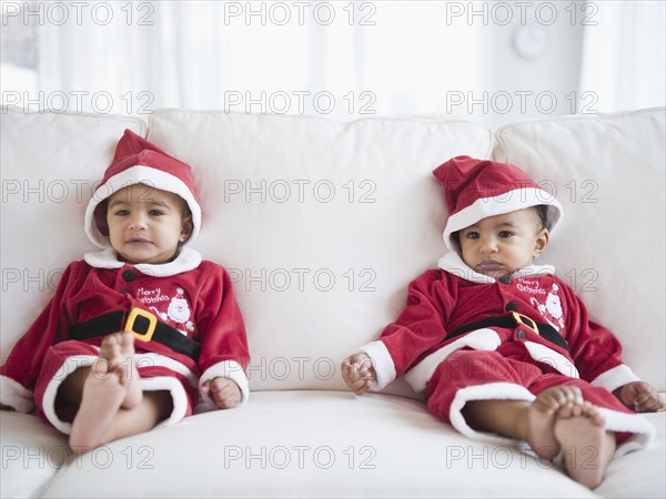 Twins on sofa dressed in Santa outfits