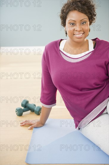 African woman sitting on yoga mat with dumbbells