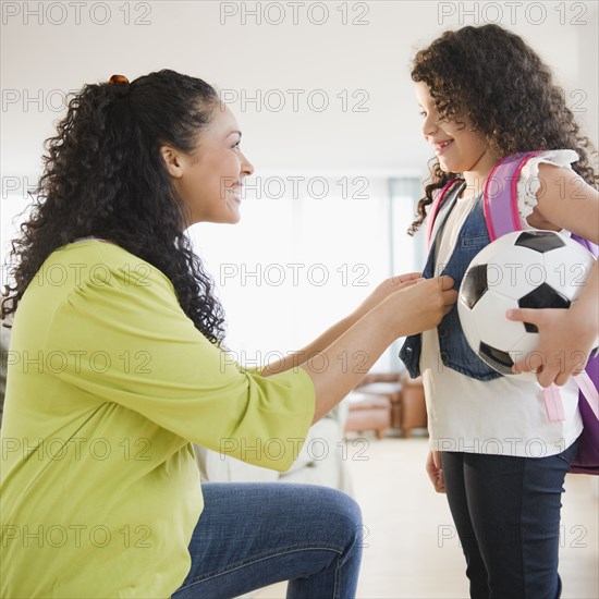 Mother dressing daughter holding soccer ball