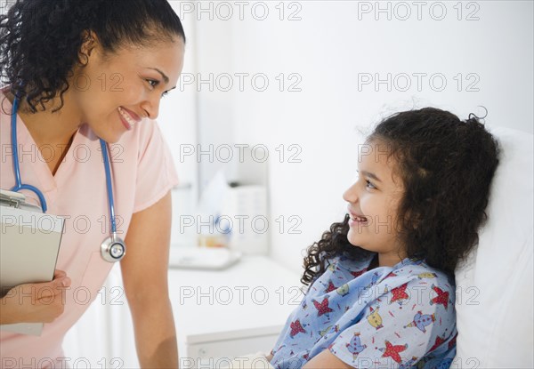 Smiling nurse talking to girl in hospital bed