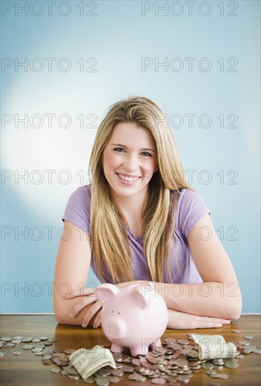 Caucasian teenage girl sitting with coins and piggy bank