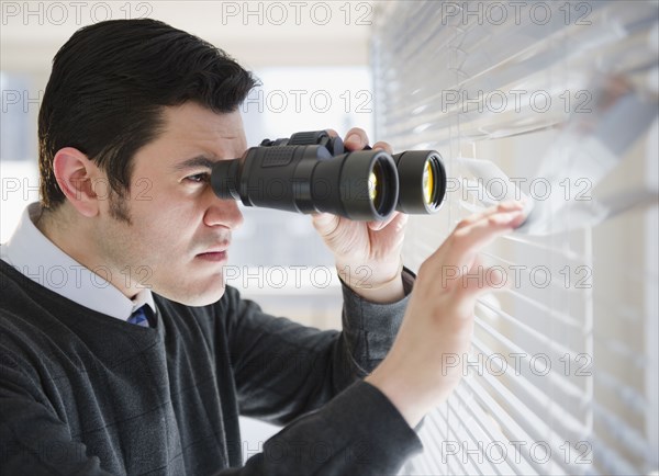 Hispanic businessman peering through window with binoculars