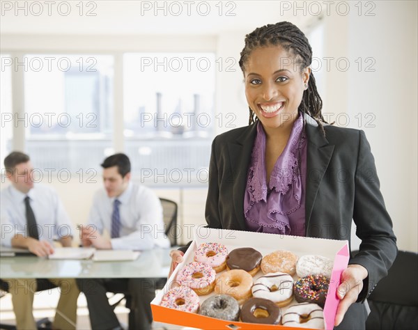 African American businesswoman carrying box of donuts
