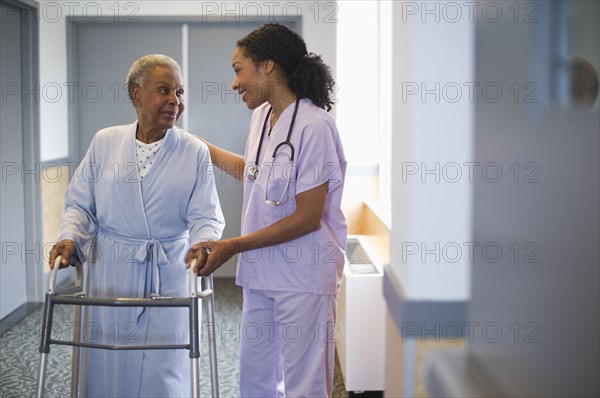 Nurse helping woman use walker in hospital hallway