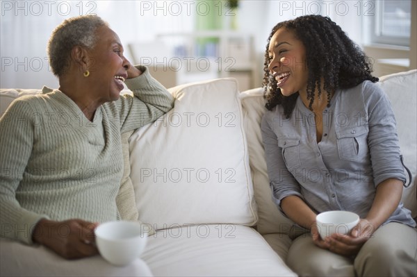 Mother and daughter talking and drinking coffee on sofa