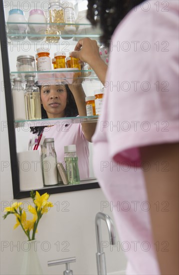 Mixed race woman taking medication from cabinet