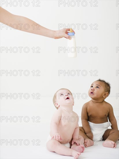 Babies looking up at hand holding bottle