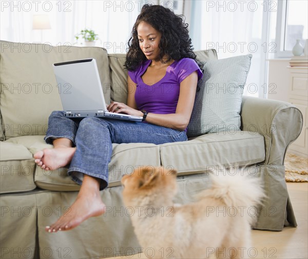 Mixed race woman sitting on sofa using laptop