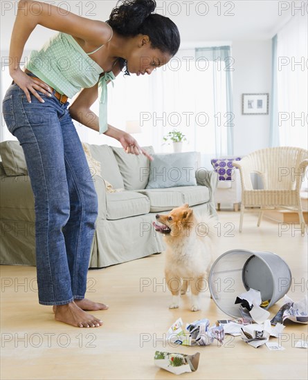 Mixed race woman scolding Pomeranian dog next to garbage