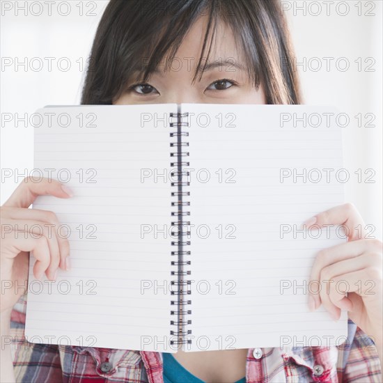Korean woman holding notebook on front of her face