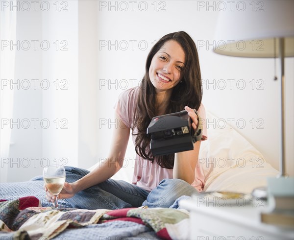 Brazilian woman sitting in bed with wine and instant camera