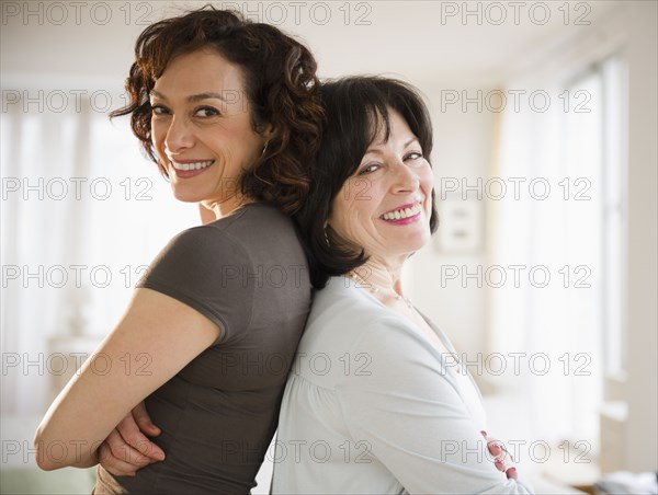 Adult daughter and mother standing back to back