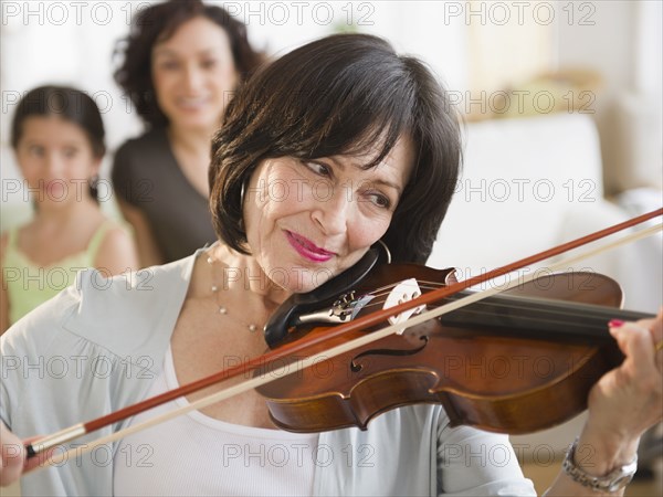 Mother and daughter watching grandmother playing violin