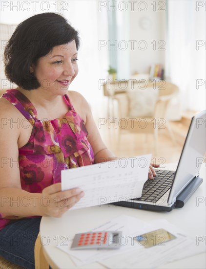 Hispanic woman holding paper and using laptop