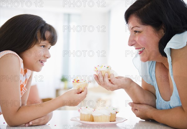 Hispanic mother and daughter eating cupcakes