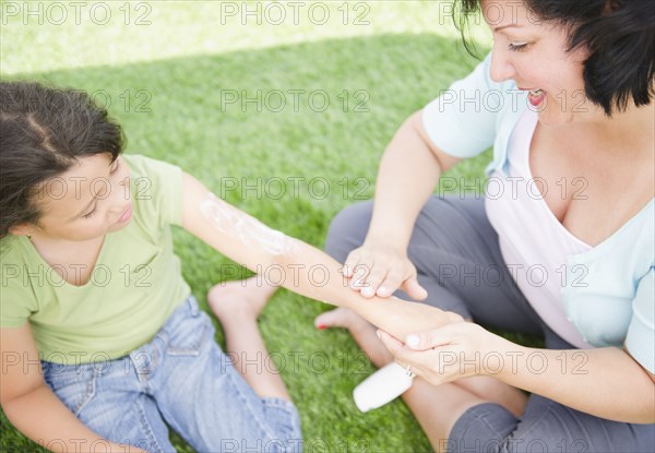 Hispanic mother putting sunscreen on daughter