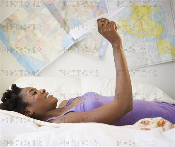 Black woman laying in bed holding paper airplane