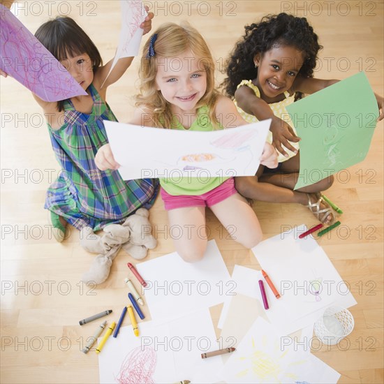 Children sitting on floor holding up drawings