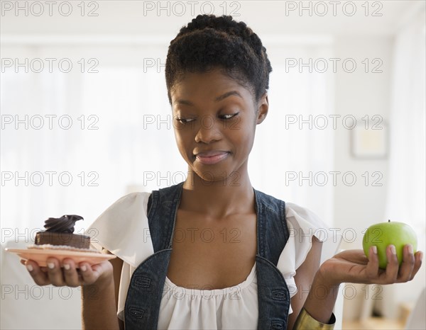 Black woman deciding between chocolate cake and apple