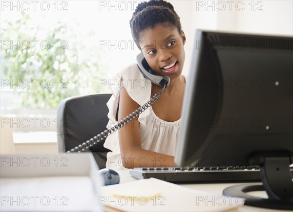 Black businesswoman talking on phone and using laptop