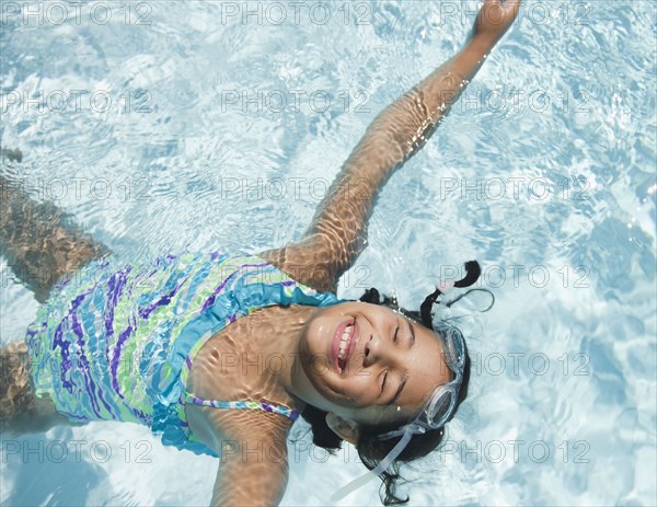 Hispanic girl floating in swimming pool