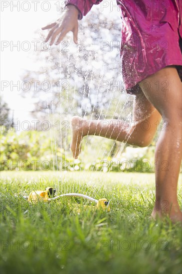 Hispanic girl running through sprinkler