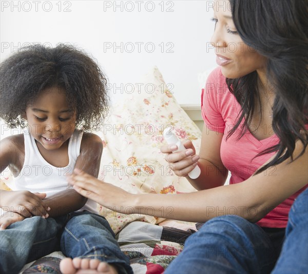 African American mother putting lotion on son