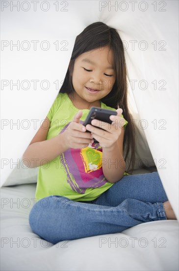 Korean girl using cell phone under sheet