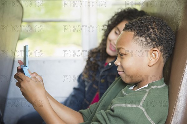 Girl watching boy playing video game on school bus