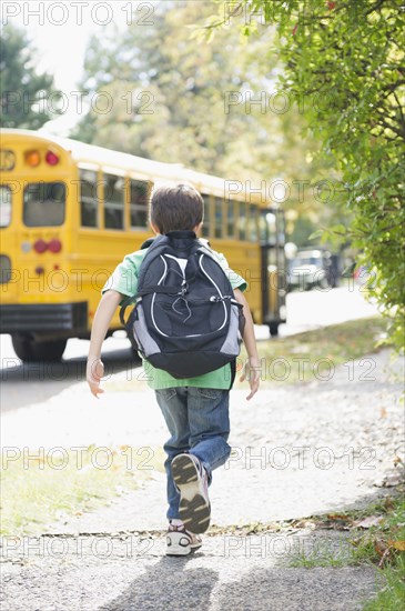 Caucasian boy running after school bus
