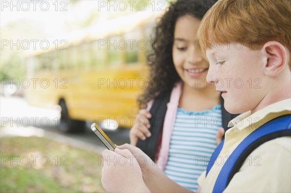 Children using cell phone while waiting for school bus