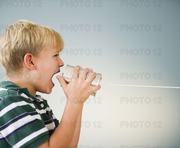 Caucasian boy shouting into tin can telephone