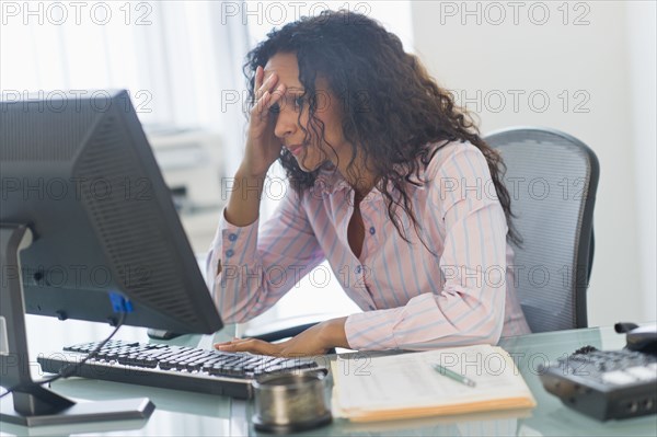 Frustrated Hispanic businesswoman using computer at desk