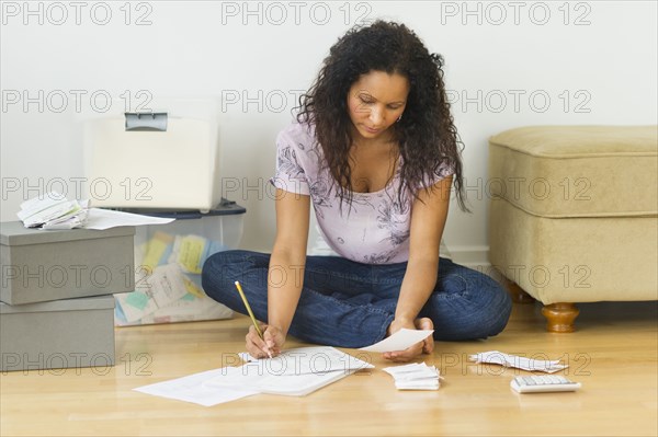 Hispanic woman sitting on floor paying bills