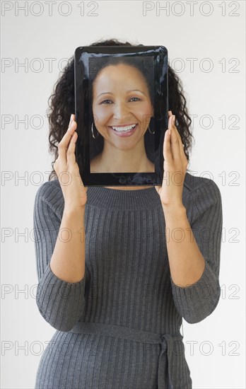 Hispanic woman holding digital tablet in front of face