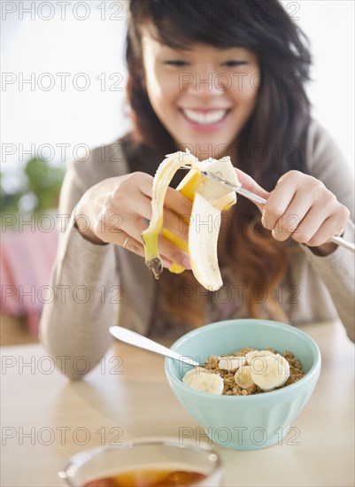 Pacific Islander woman putting bananas on cereal