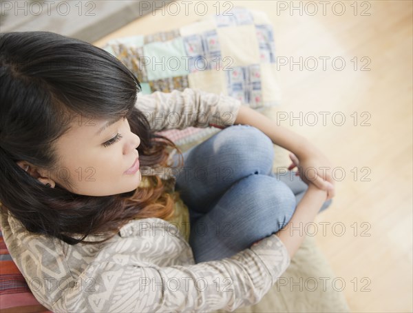 Pacific Islander woman thinking and sitting on sofa