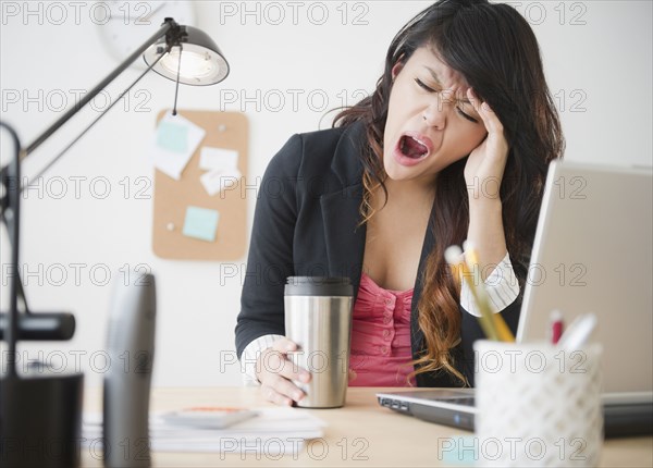 Pacific Islander businesswoman yawning at desk