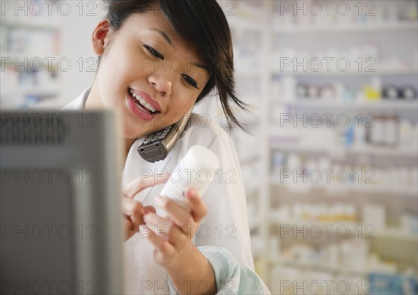 Pacific Islander pharmacist reviewing medication and talking on telephone