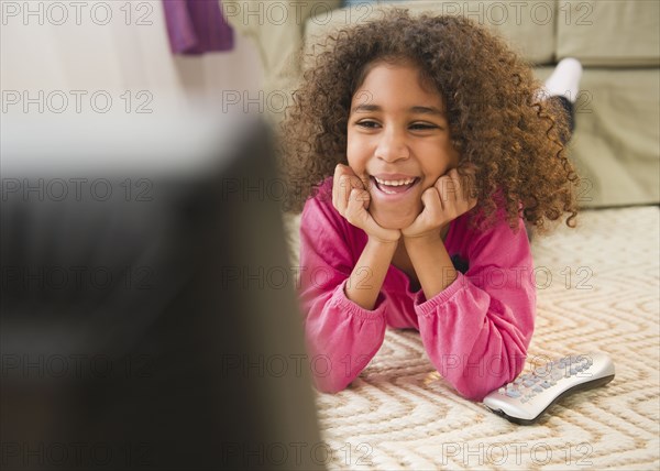 Mixed race girl laying on floor watching television