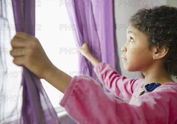 Mixed race girl opening curtains