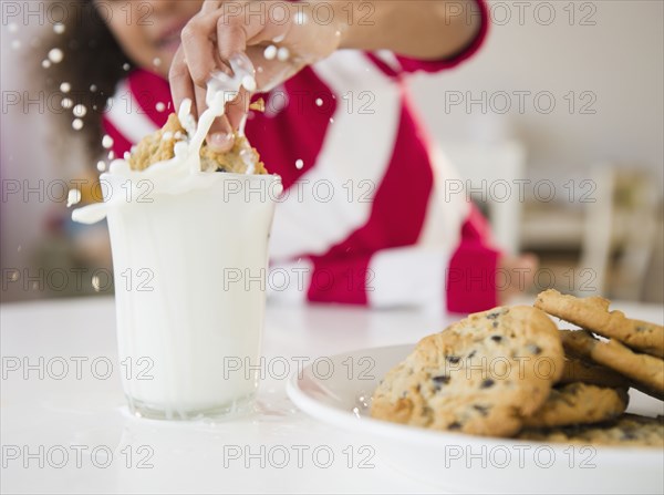 Mixed race girl dunking cookie into milk