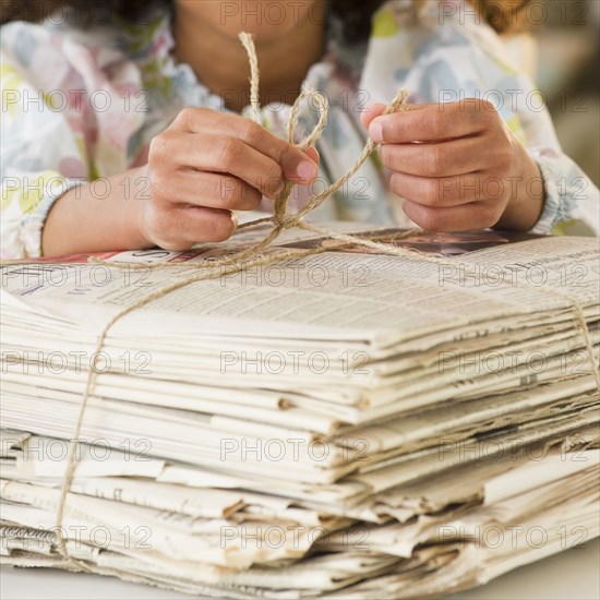 Mixed race girl tying bundle of newspapers