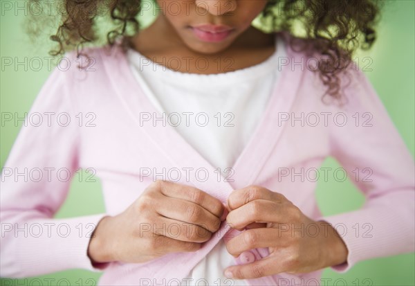 Mixed race girl buttoning sweater