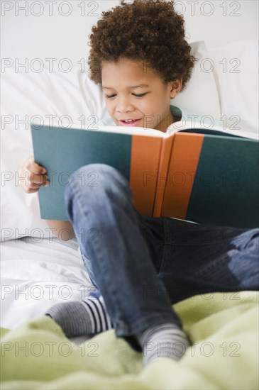 Black boy reading book in bed
