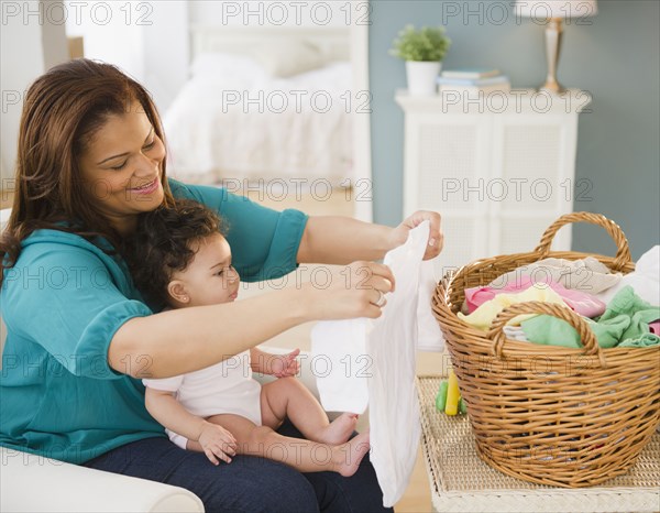 Mixed race mother folding laundry and holding baby