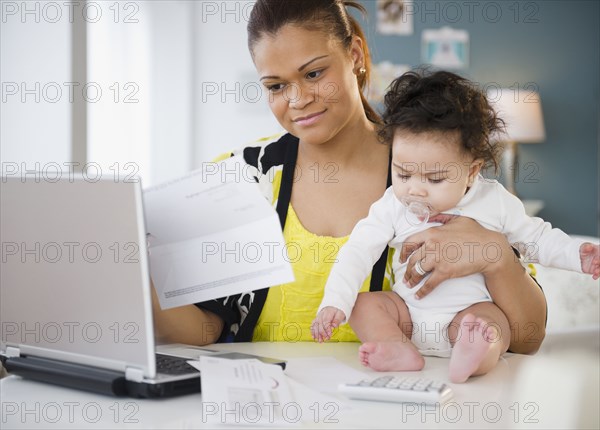 Mixed race mother holding baby and paying bills
